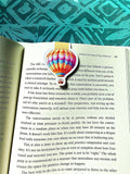 Colorful hot air balloon bookmark on an open book with a patterned green background