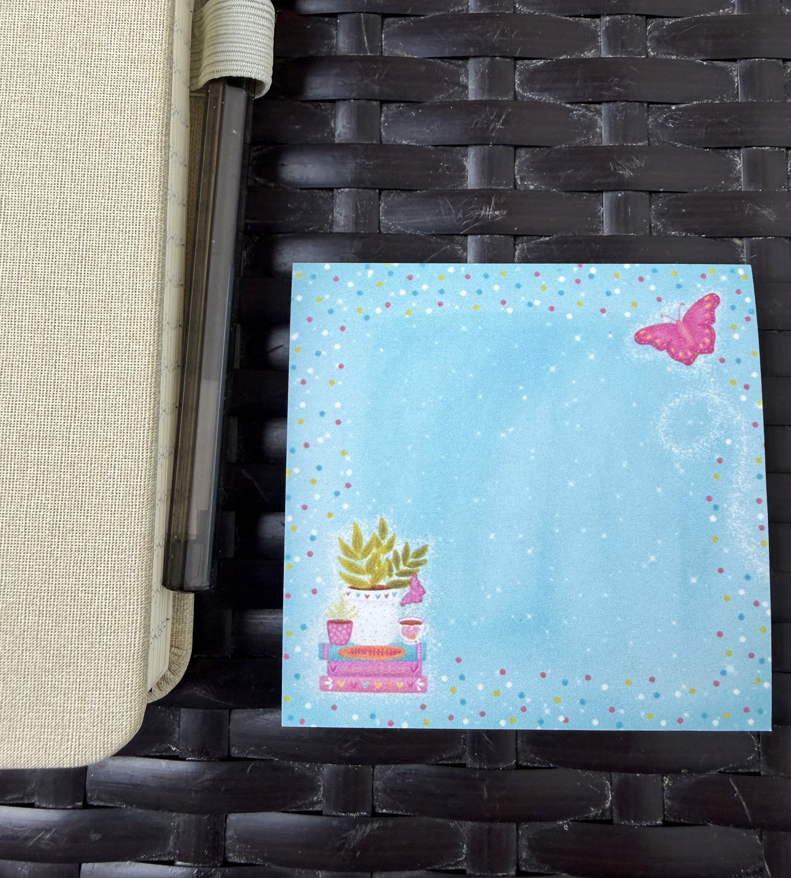 "3x3 inch sticky note by Emily Cromwell Designs featuring a cozy book stack, potted plants, and a pink butterfly on a whimsical blue background."