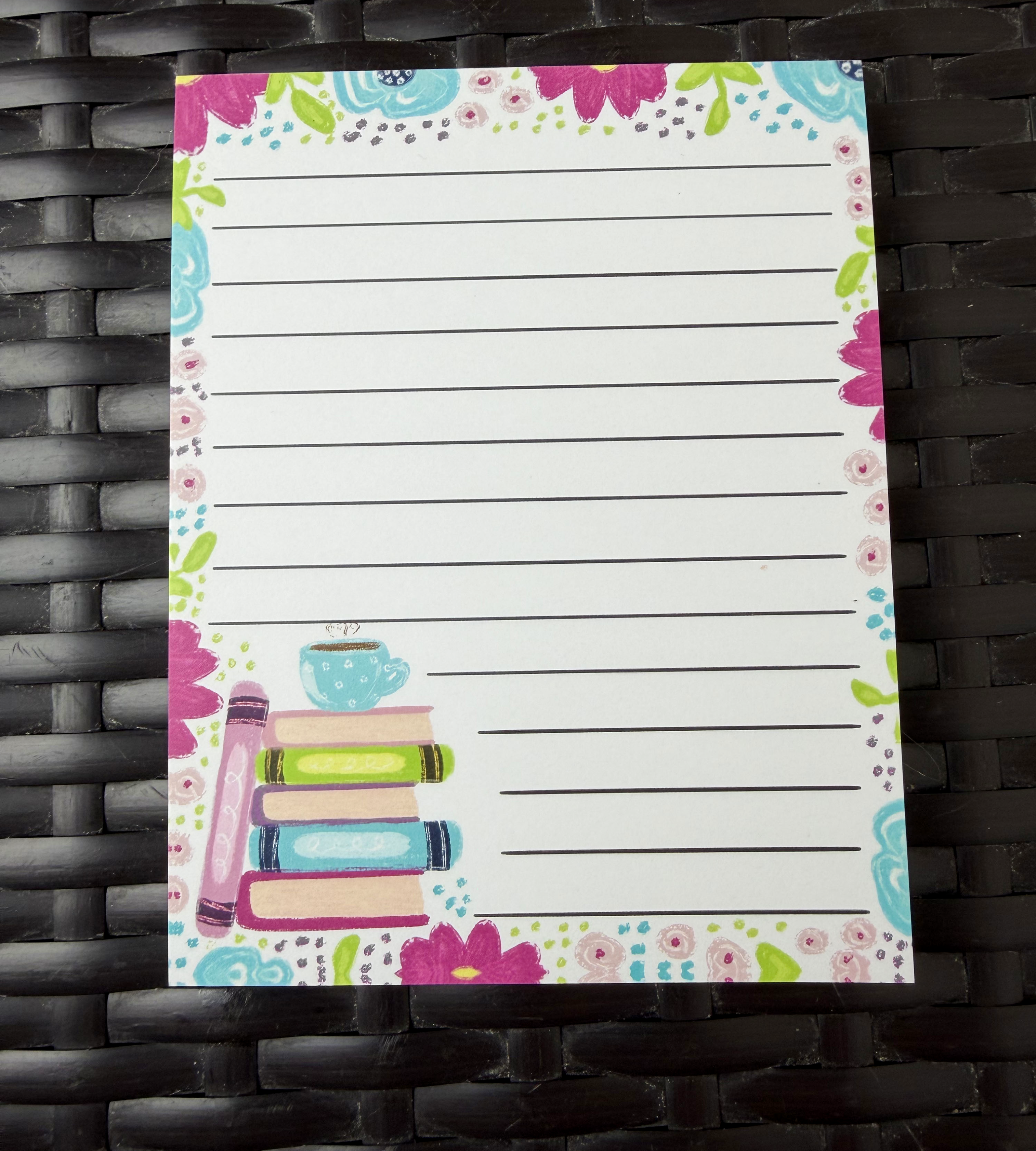 Notepad with colorful floral border and book illustration on a woven surface