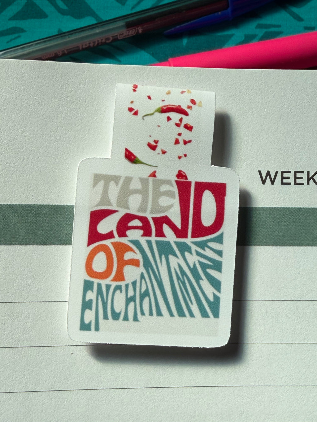 Colorful magnetic bookmark with the text "Land of Enchantment" on a notebook page.
