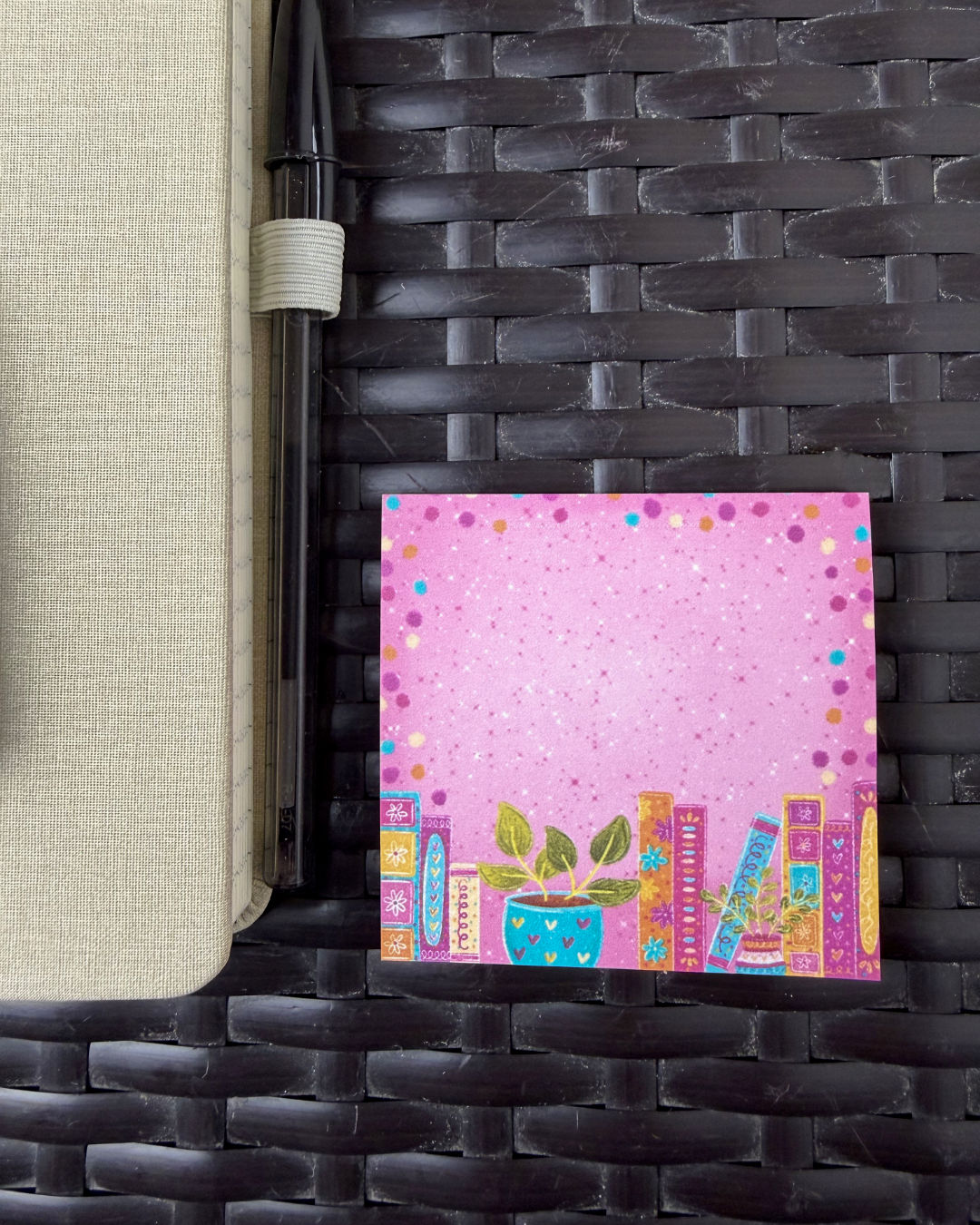 Pink notepad with colorful designs on a woven surface