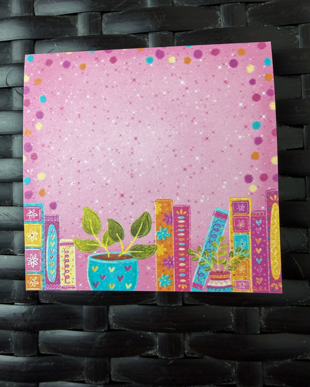 Colorful card with plants and text on a pink background, against a black woven background.