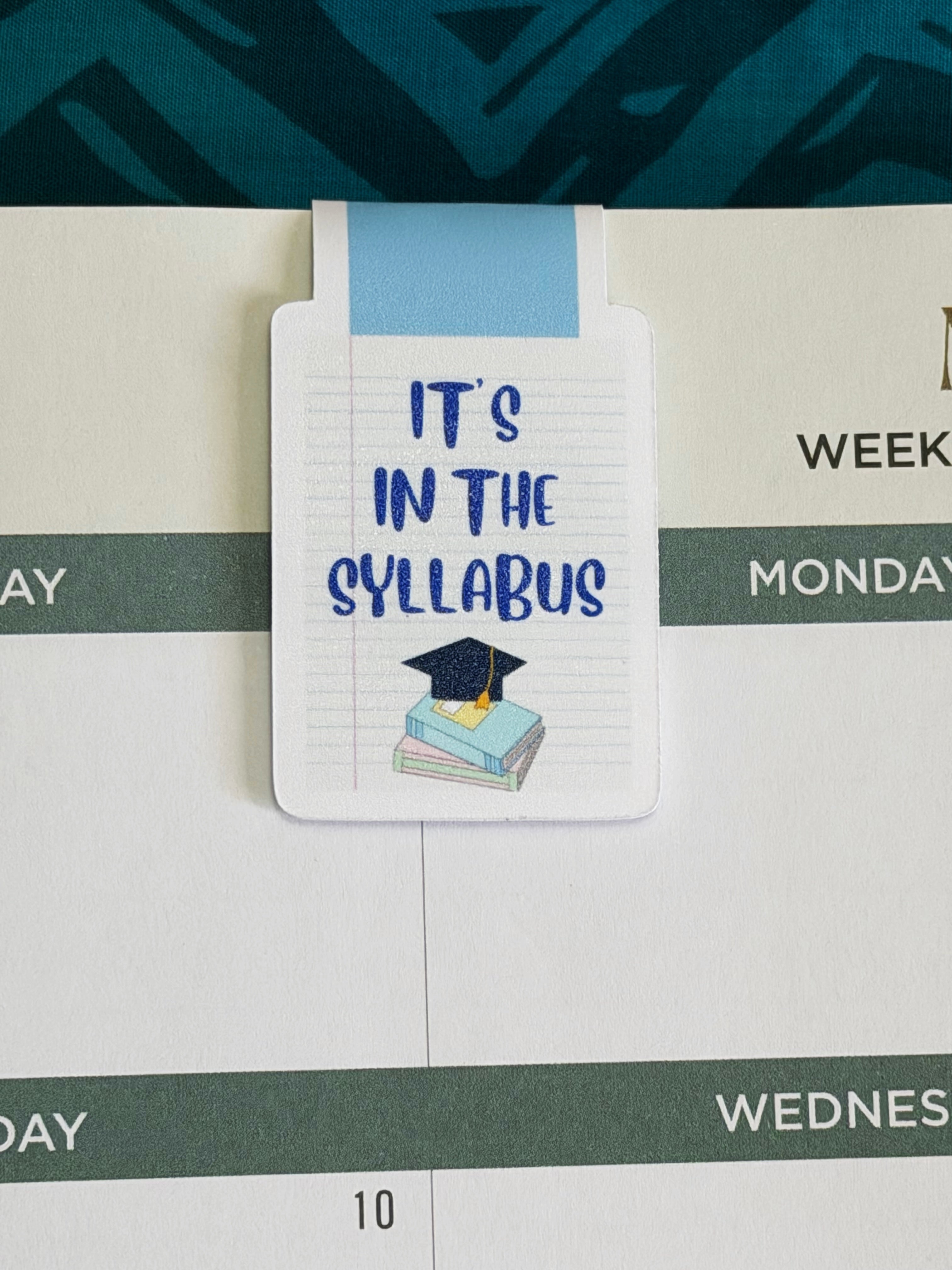 Notebook with 'It's in the Syllabus' sticker on a calendar